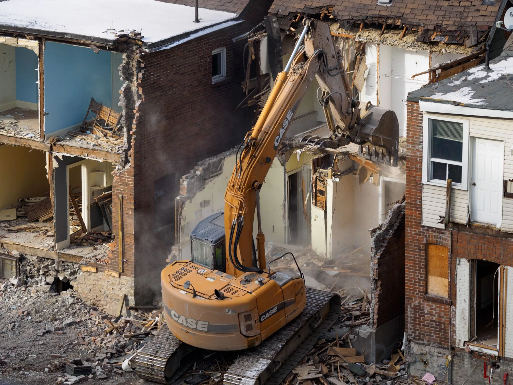 An excavator demolishing a brick building at a construction site.